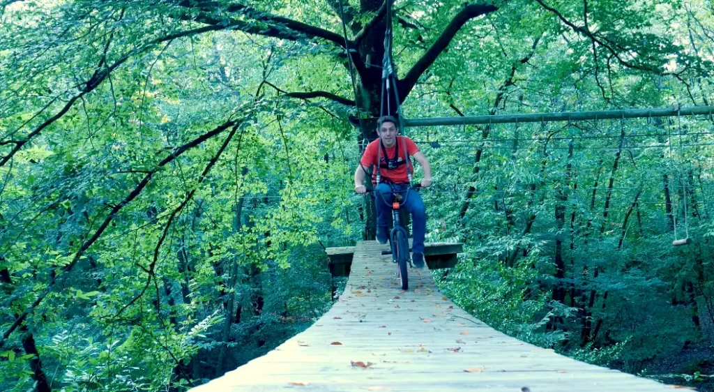Homme faisant du vélo sur un pont suspendu entre deux arbres
